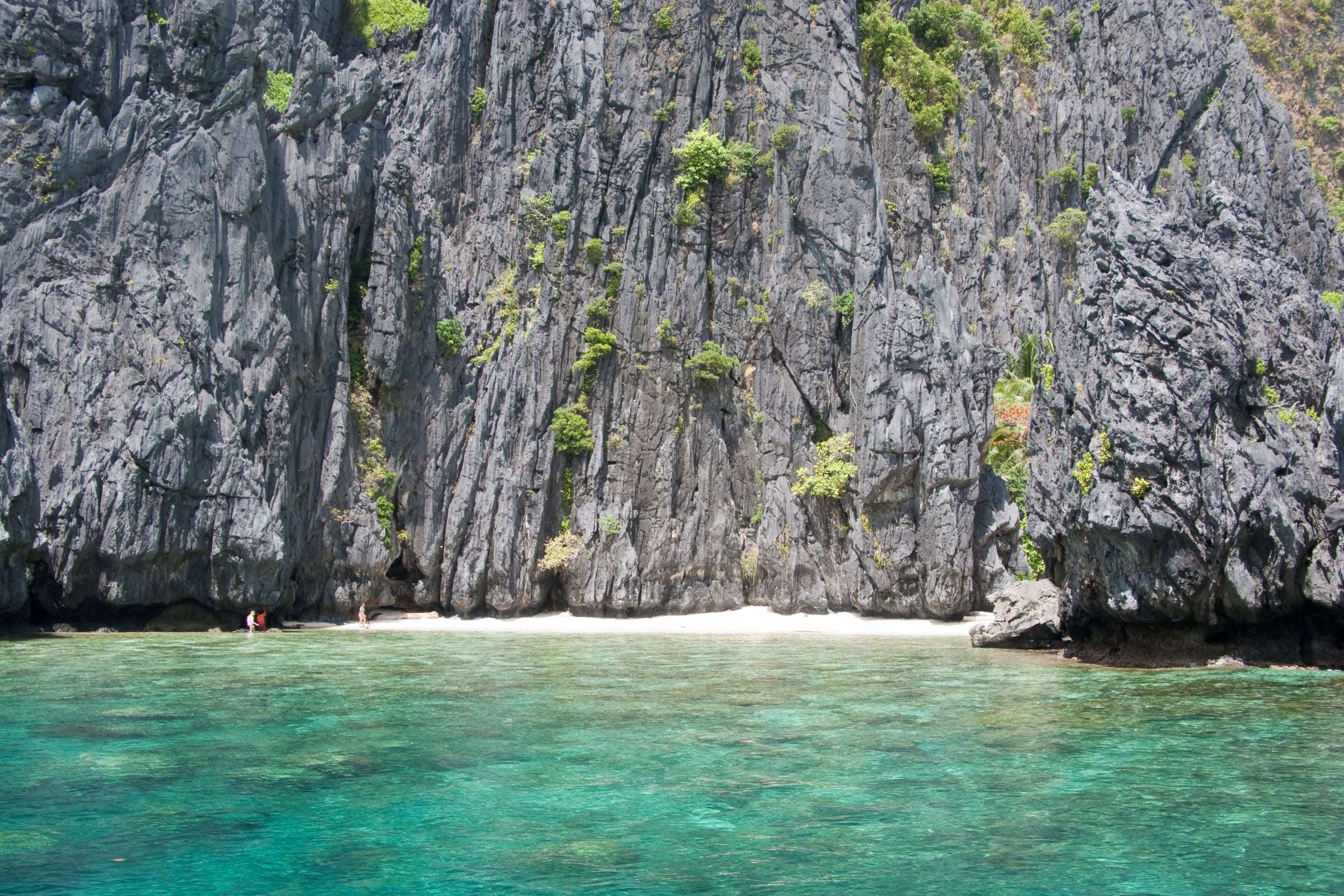 Island lagoon with steep green cliffs and clear shallow water in Bacuit Bay, El Nido