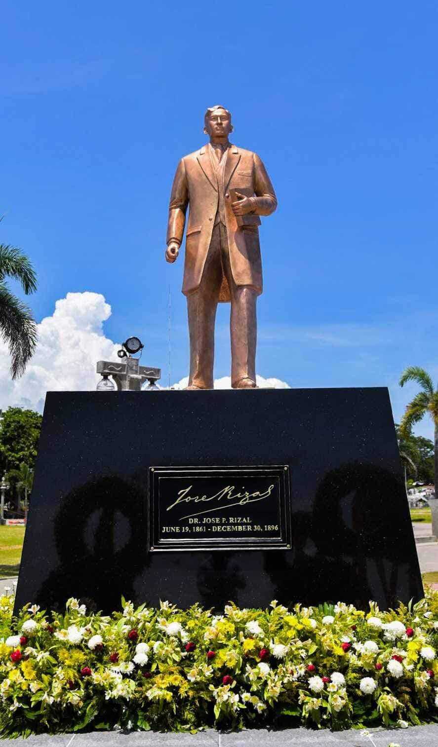 Bronze statue of Dr. José Rizal at Rizal Boulevard Dumaguete with engraved plaque and tropical garden under blue sky