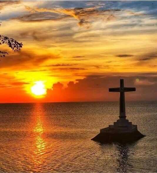 Camiguin Sunken Cemetery white cross silhouetted against golden sunset over the sea
