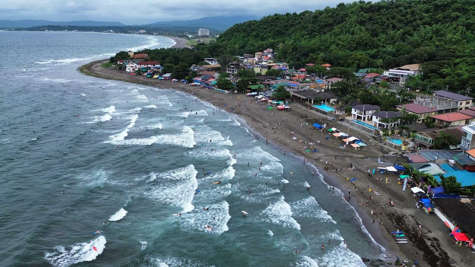 Aerial view of Urbiztondo Beach La Union surfers in the waves and resorts along the curving coastline