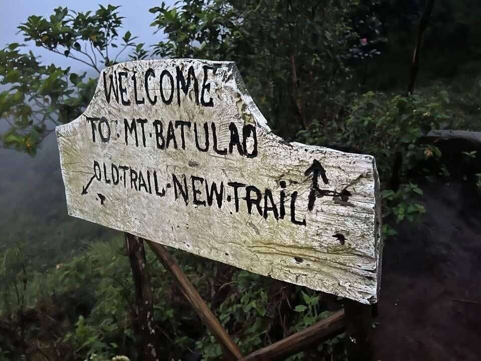 Mt. Batulao Batangas weathered wooden trail sign welcoming hikers with arrows pointing to Old Trail and New Trail at misty mountain trailhead