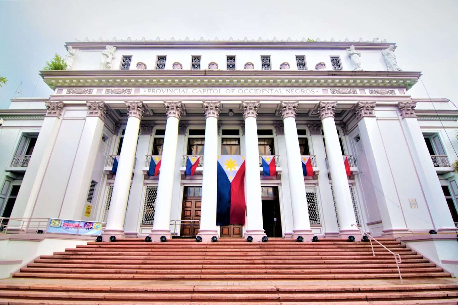 Bacolod Provincial Capitol of Occidental Negros neoclassical white building with Corinthian columns and Philippine flags draped on facade