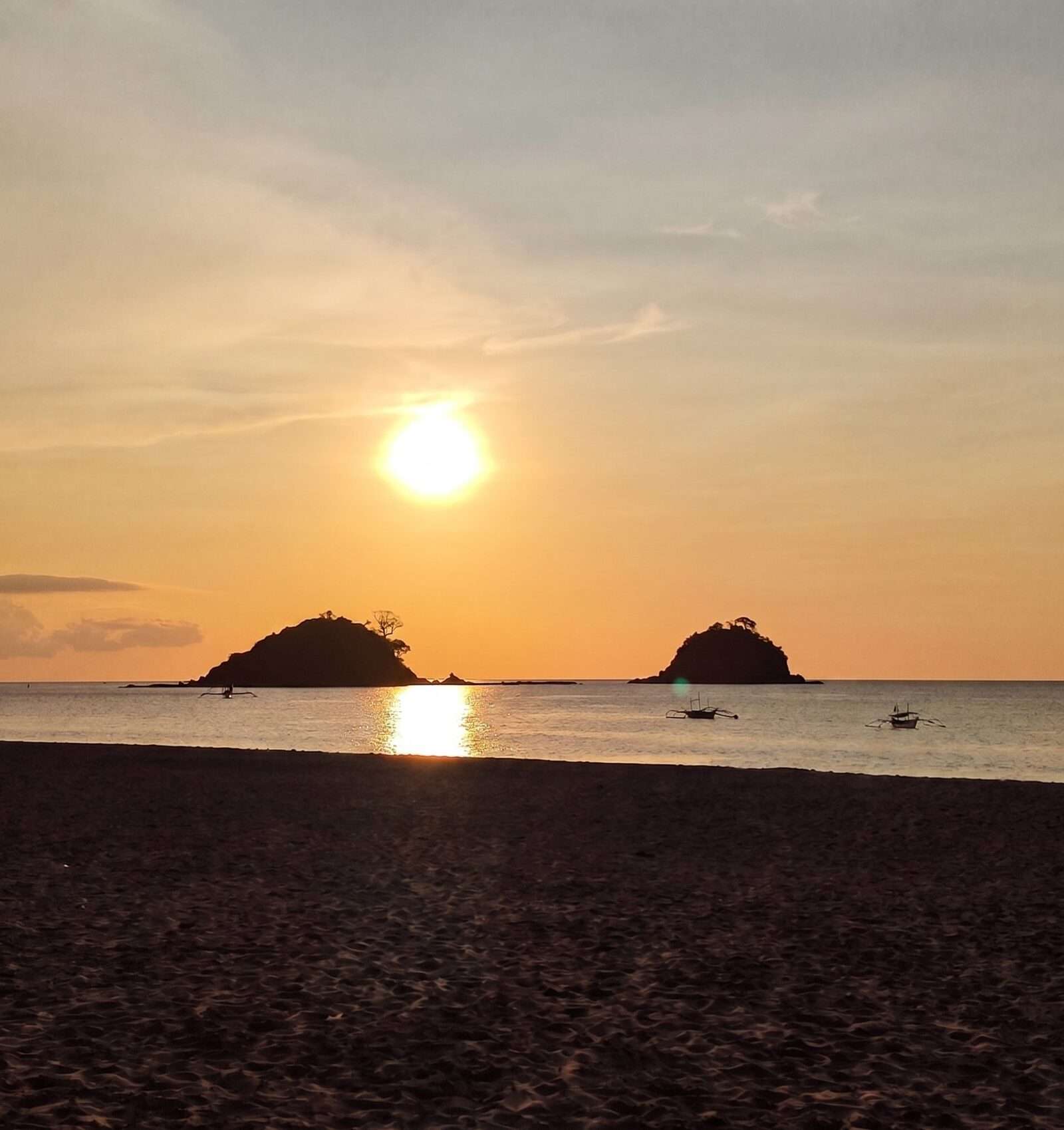 Sunset over Nacpan Beach El Nido with twin islands silhouetted on the horizon and outrigger boats in the calm water
