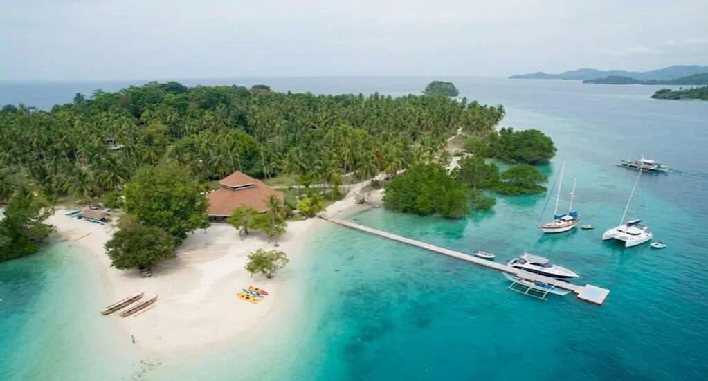 Aerial view of Samal Island near Davao with white sand beach palm trees and boats in clear turquoise water