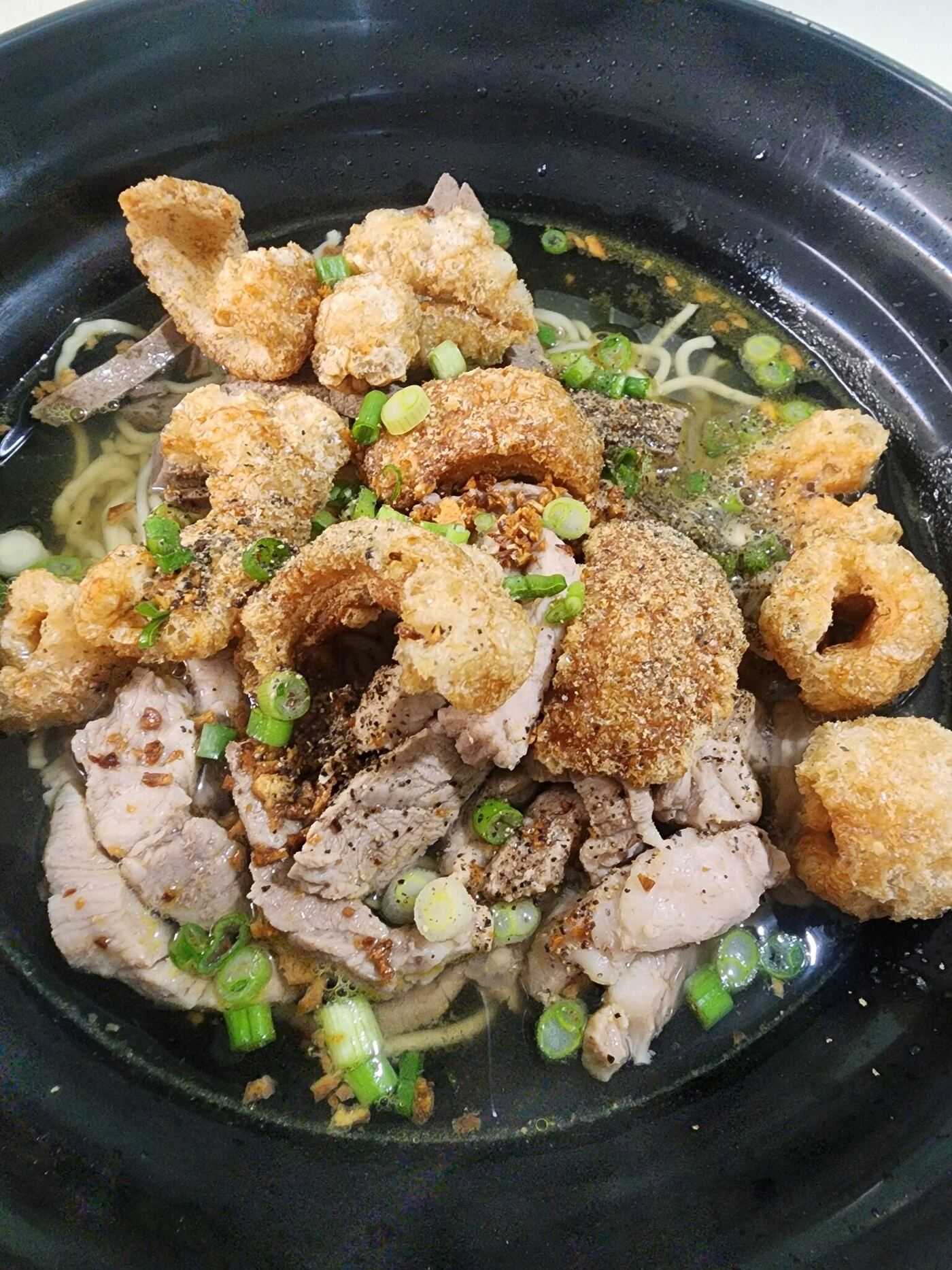 Authentic La Paz Batchoy Iloilo signature noodle soup with crispy chicharon, sliced pork, scallions, and rich pork bone broth in black bowl