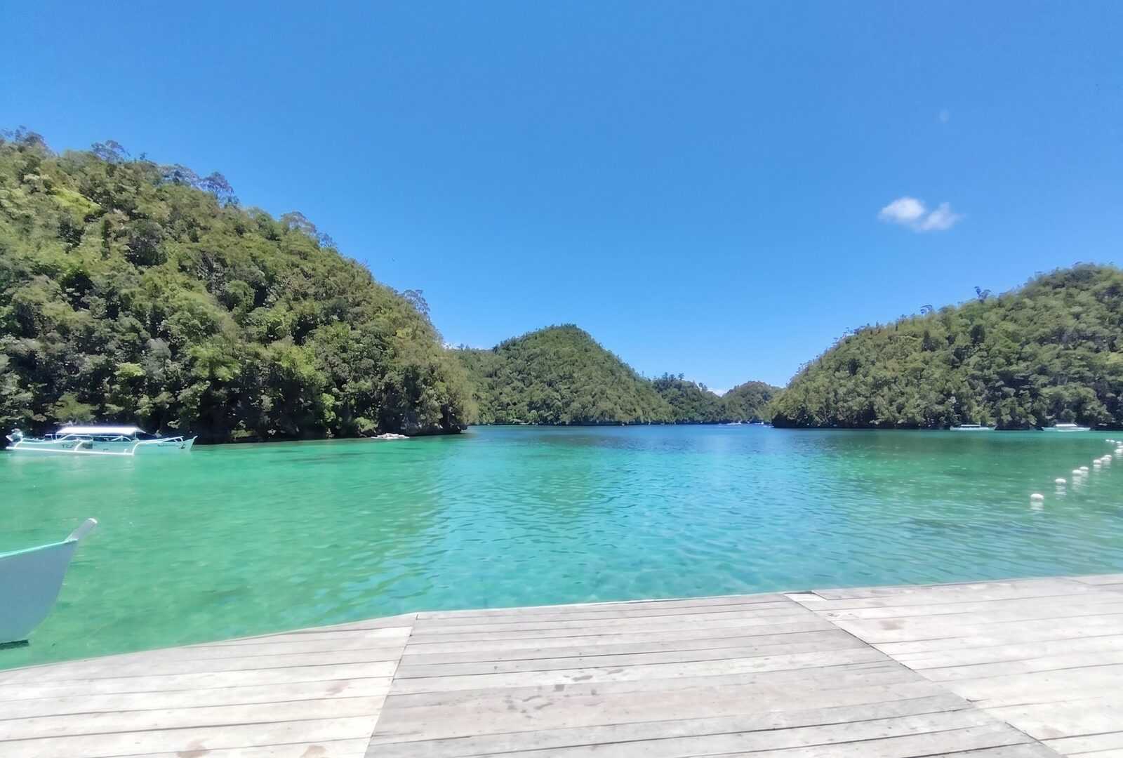Sugba Lagoon Siargao turquoise water surrounded by jungle-covered hills with wooden deck and outrigger boats